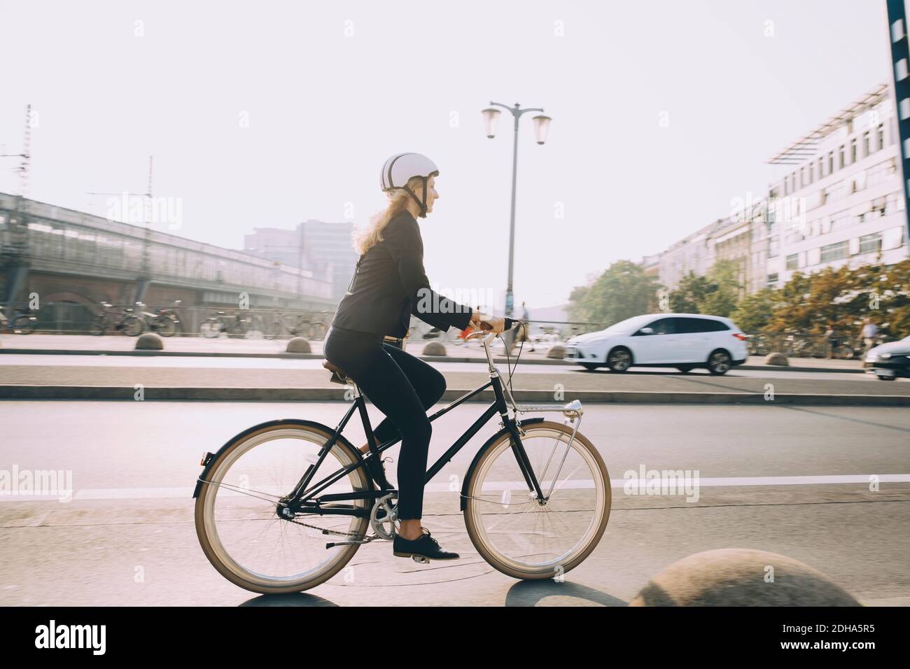 Full length of female executive wearing helmet riding bicycle on road in city Stock Photo