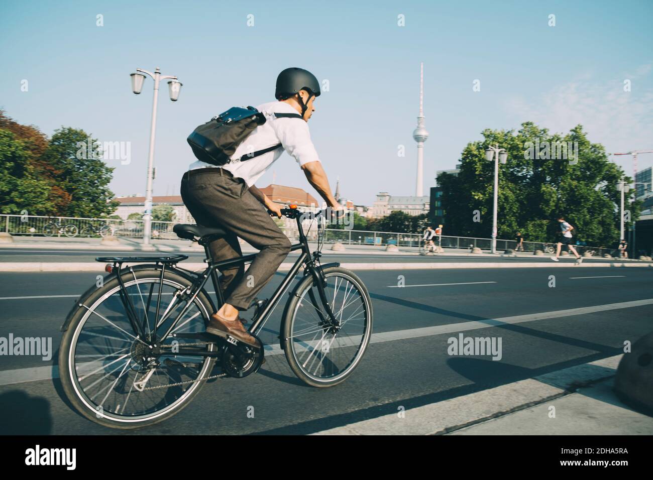 Businessman wearing helmet riding bicycle on road in city against sky Stock Photo