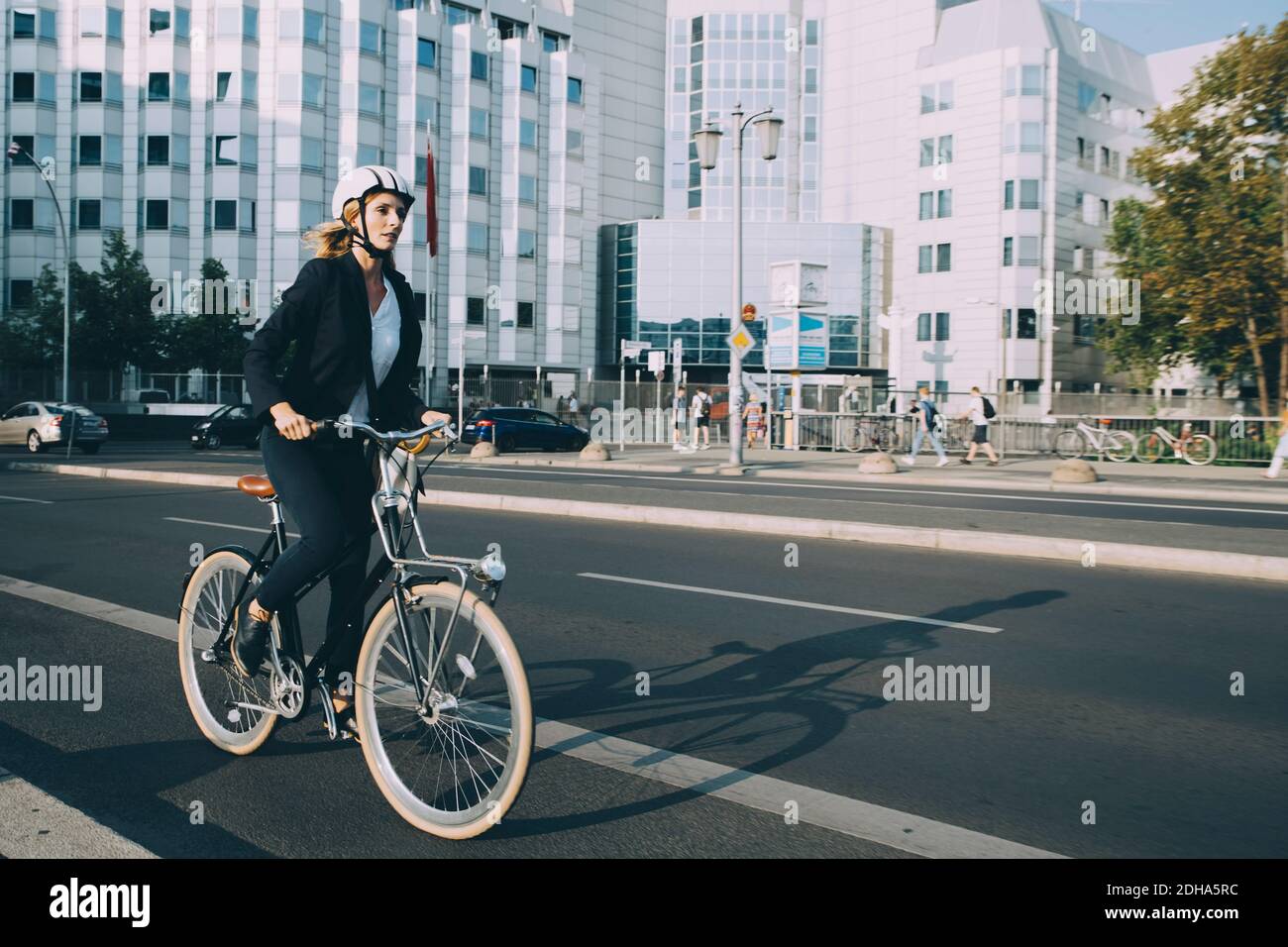 Full length of young woman wearing helmet riding bicycle on street in city Stock Photo