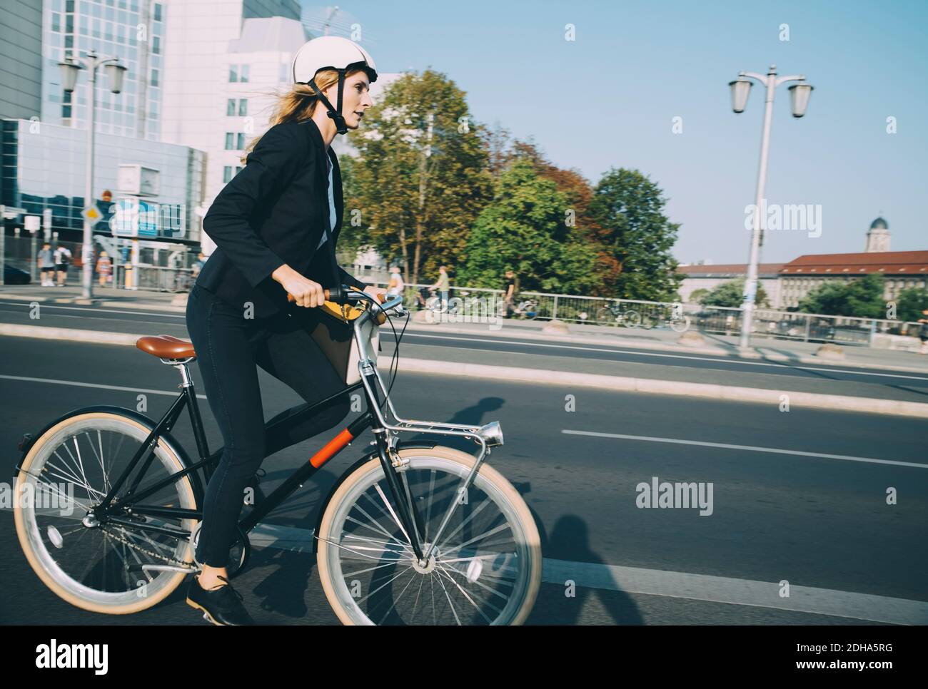 Side view of businesswoman riding bicycle on city street against sky Stock Photo