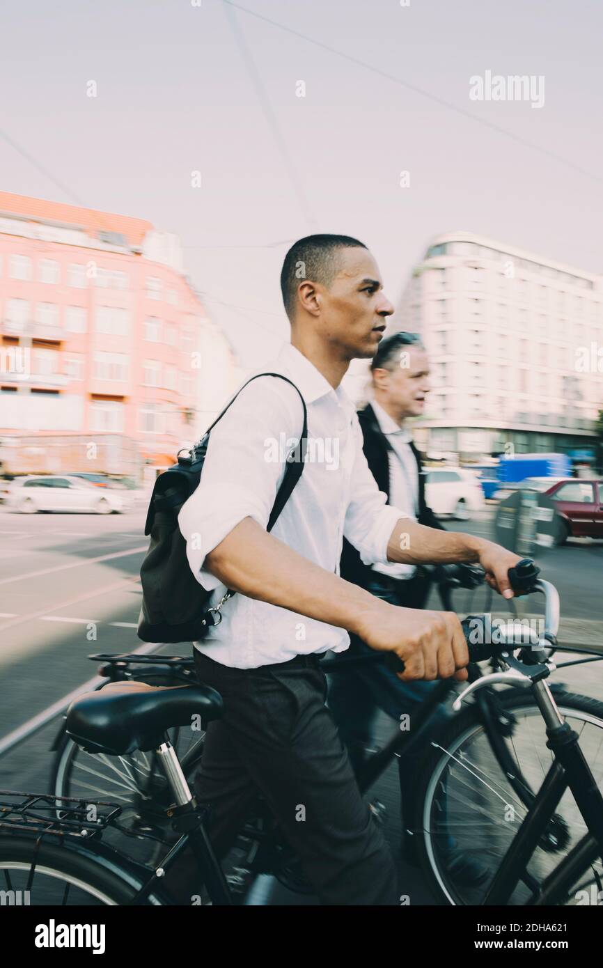 Male entrepreneurs riding bicycle on street in city against sky Stock Photo