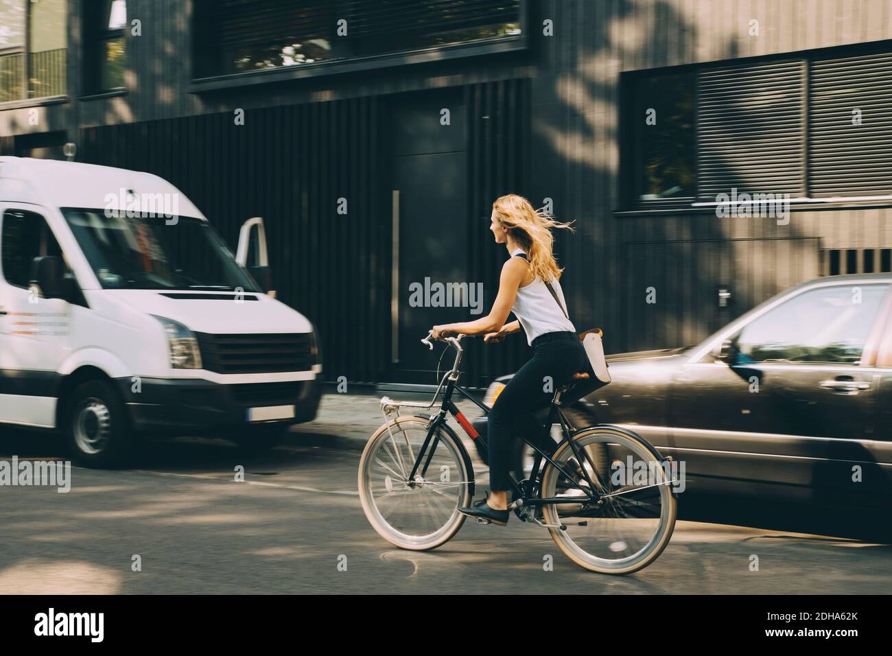 Full length of female entrepreneur riding bicycle on road in city Stock Photo