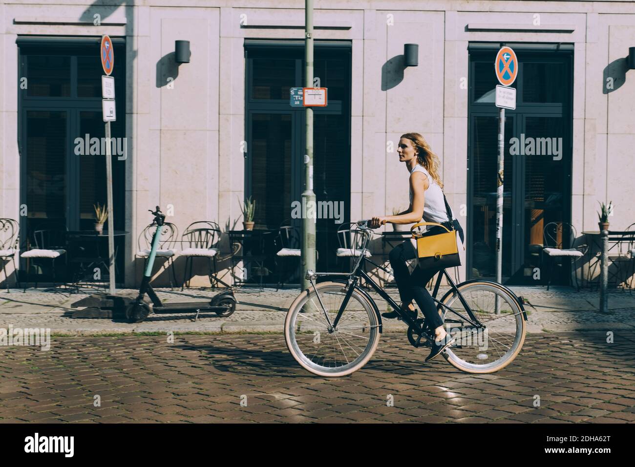 Full length of businesswoman riding bicycle against building on street in city Stock Photo