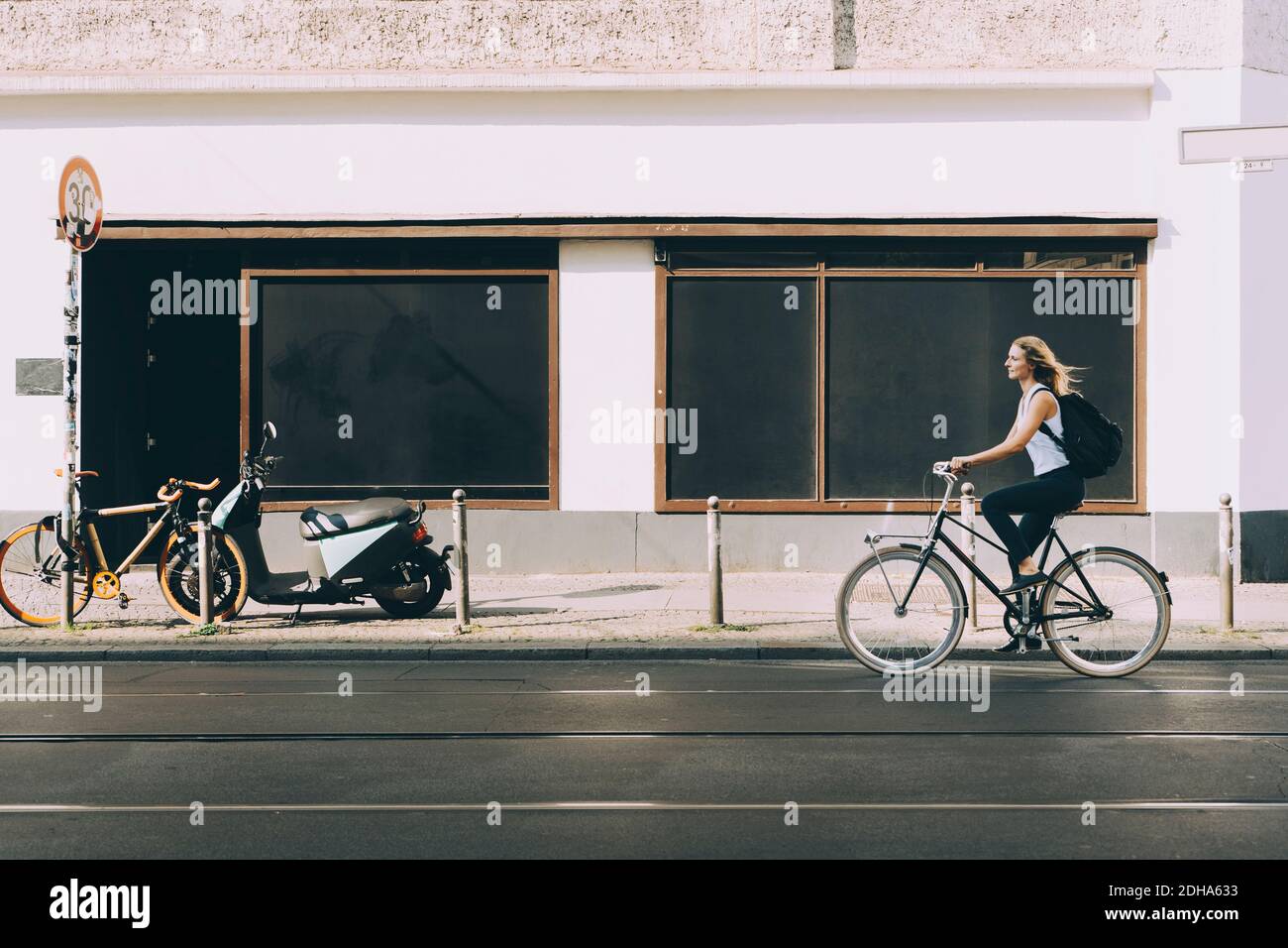 Full length of female executive riding bicycle on road against building in city Stock Photo