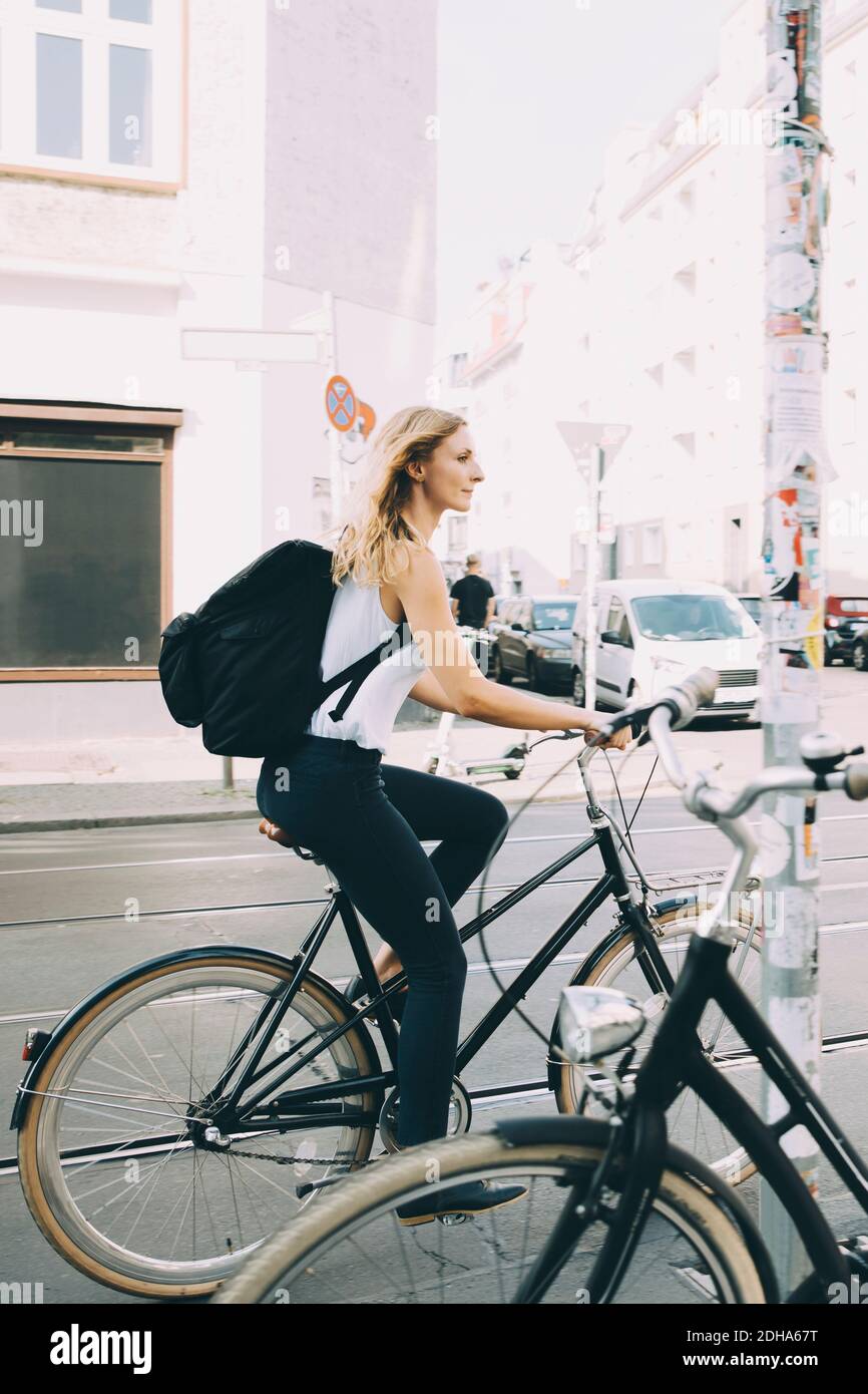Side view of young woman riding bicycle on street in city Stock Photo
