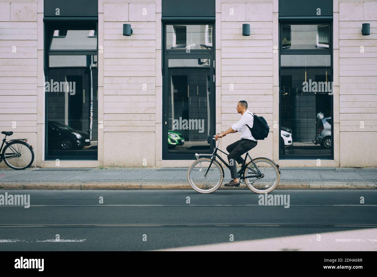 Full length of businessman riding bicycle on street against building in city Stock Photo