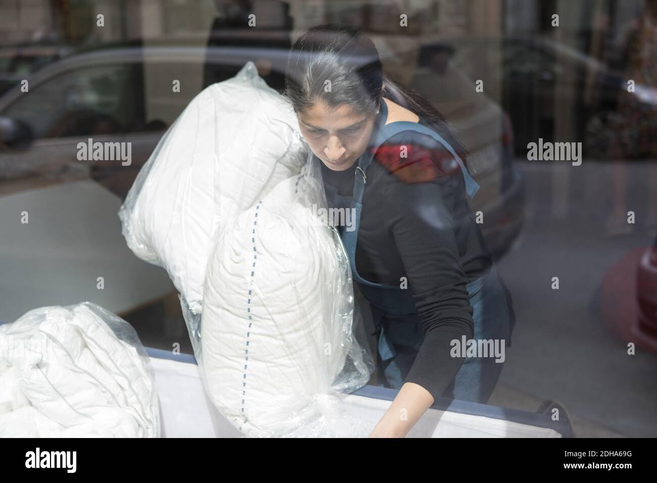 Mature female dry cleaner carrying pillows seen from Laundromat window