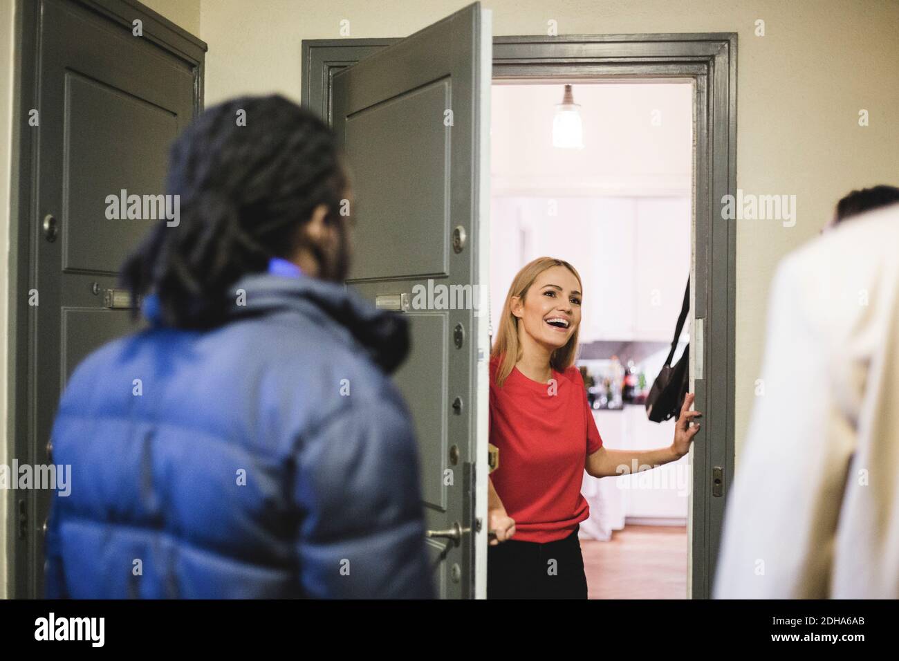 Cheerful woman greeting friends while standing at doorway Stock Photo