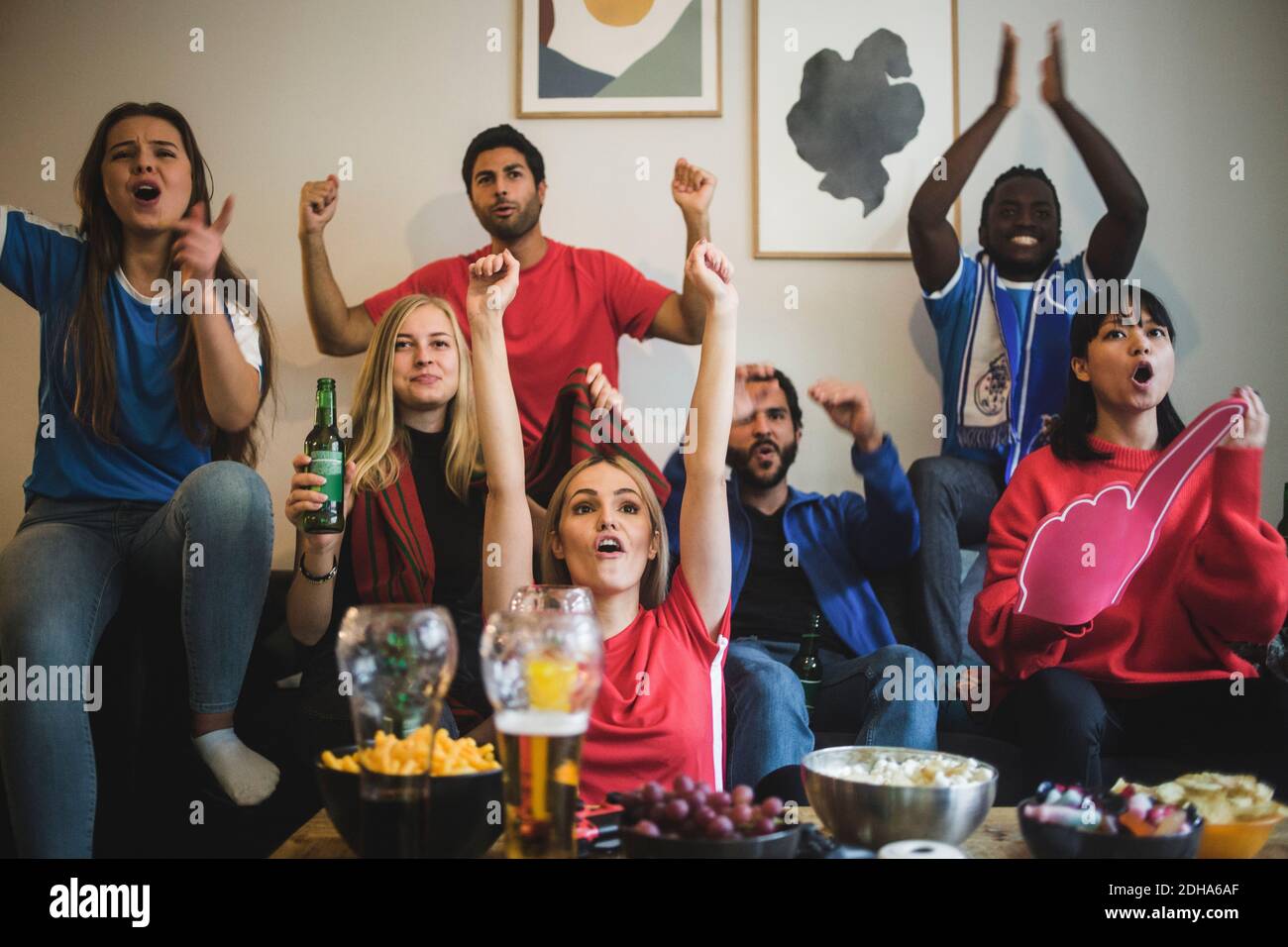 Happy friends with arms raised watching sport while sitting on sofa at home Stock Photo