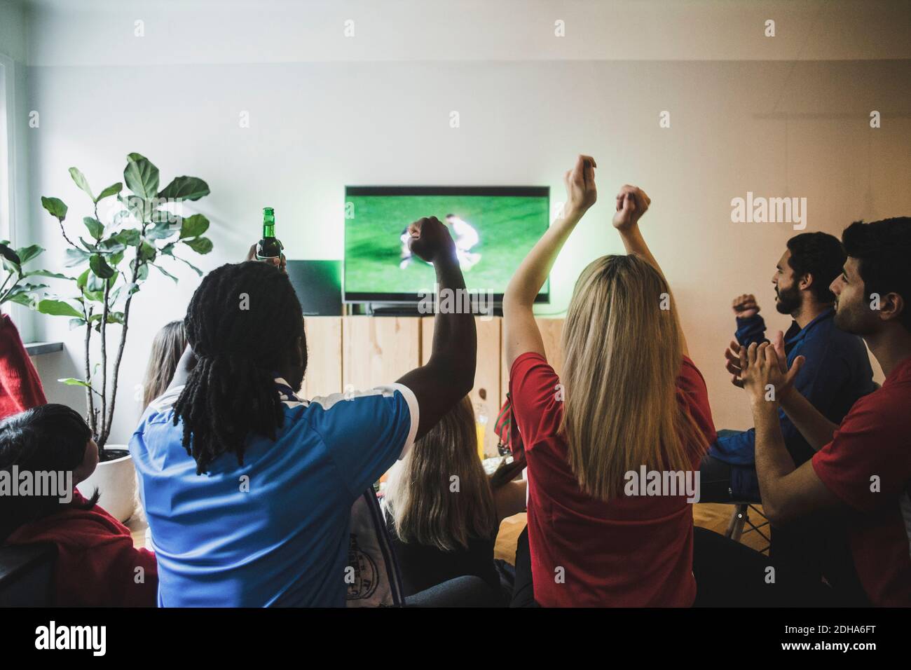 Cheerful friends with arms raised watching soccer match in living room Stock Photo