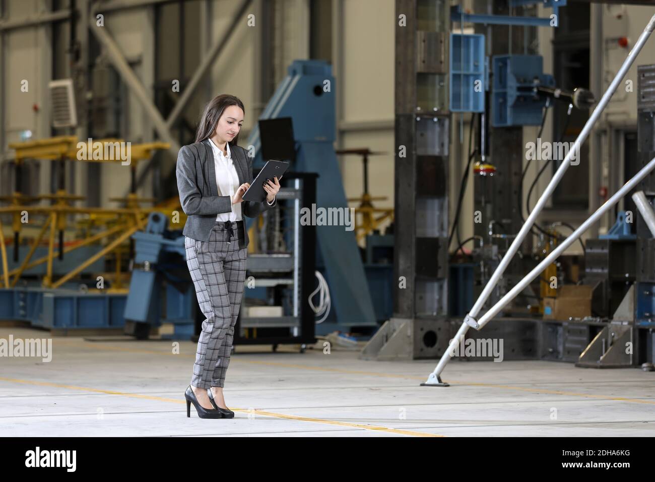 Young female businesswoman in a business suit and black glasses with a tablet and smartphone, controlling work process in a factory. Stock Photo