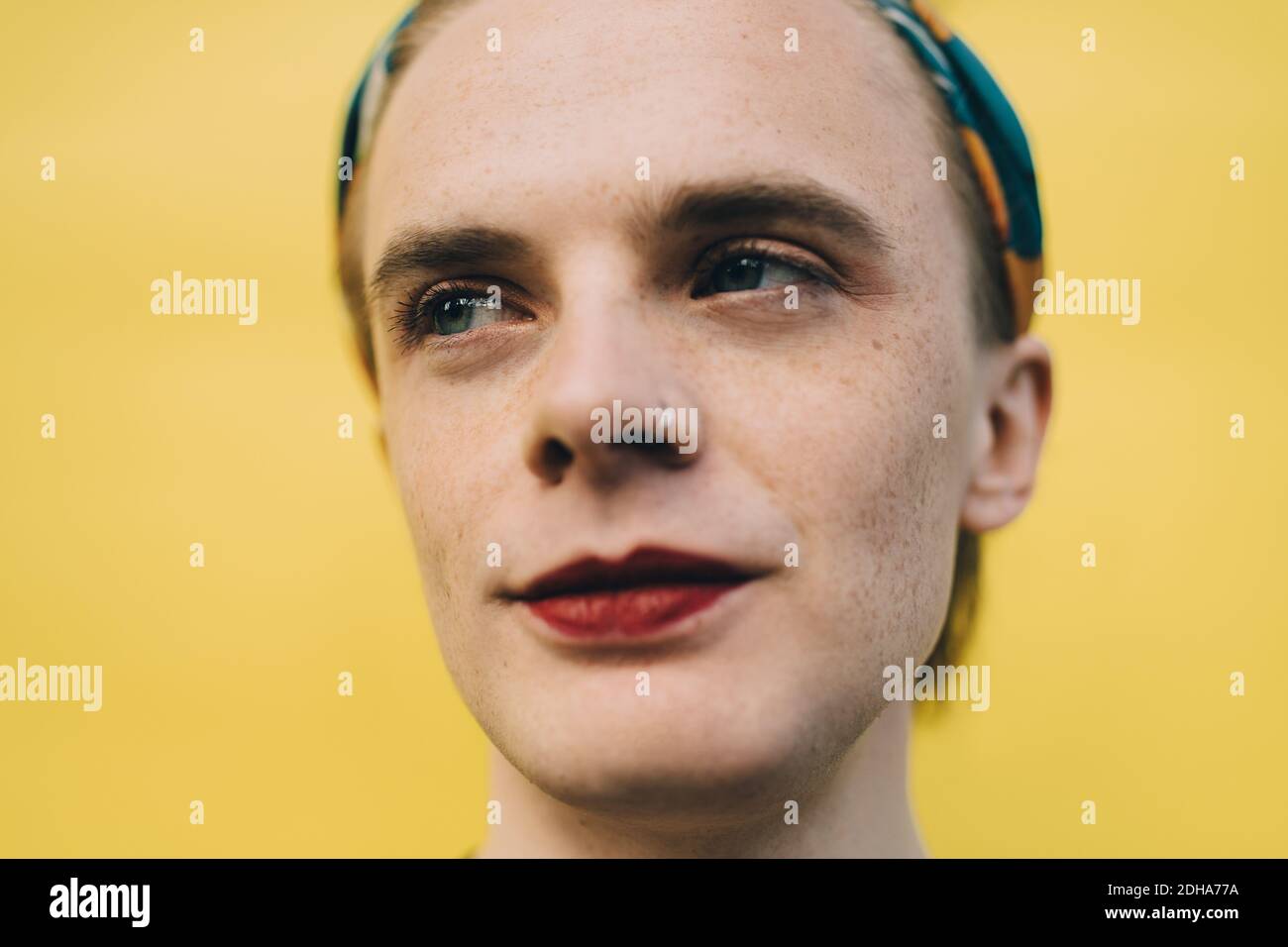 Smiling young man looking away while standing against yellow background Stock Photo
