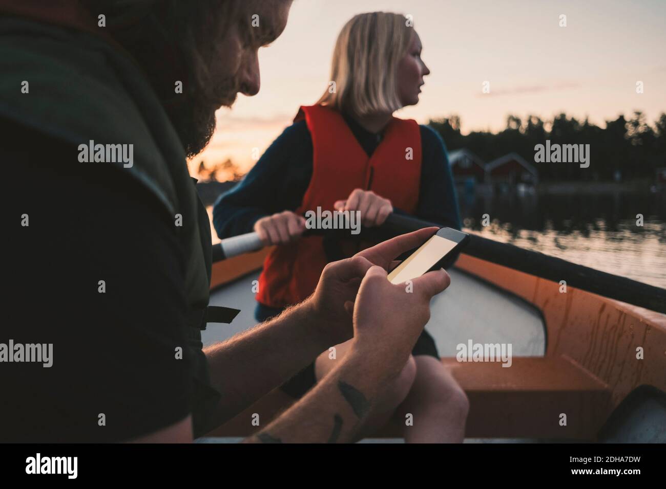 Man using mobile phone while woman rowing boat on lake Stock Photo