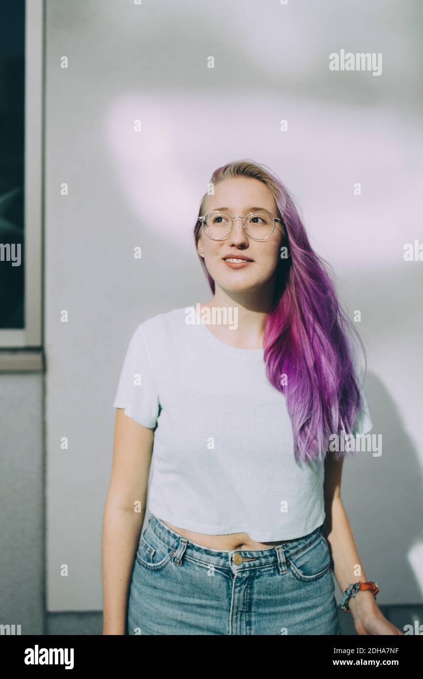 Smiling teenage girl looking away while standing against wall Stock ...