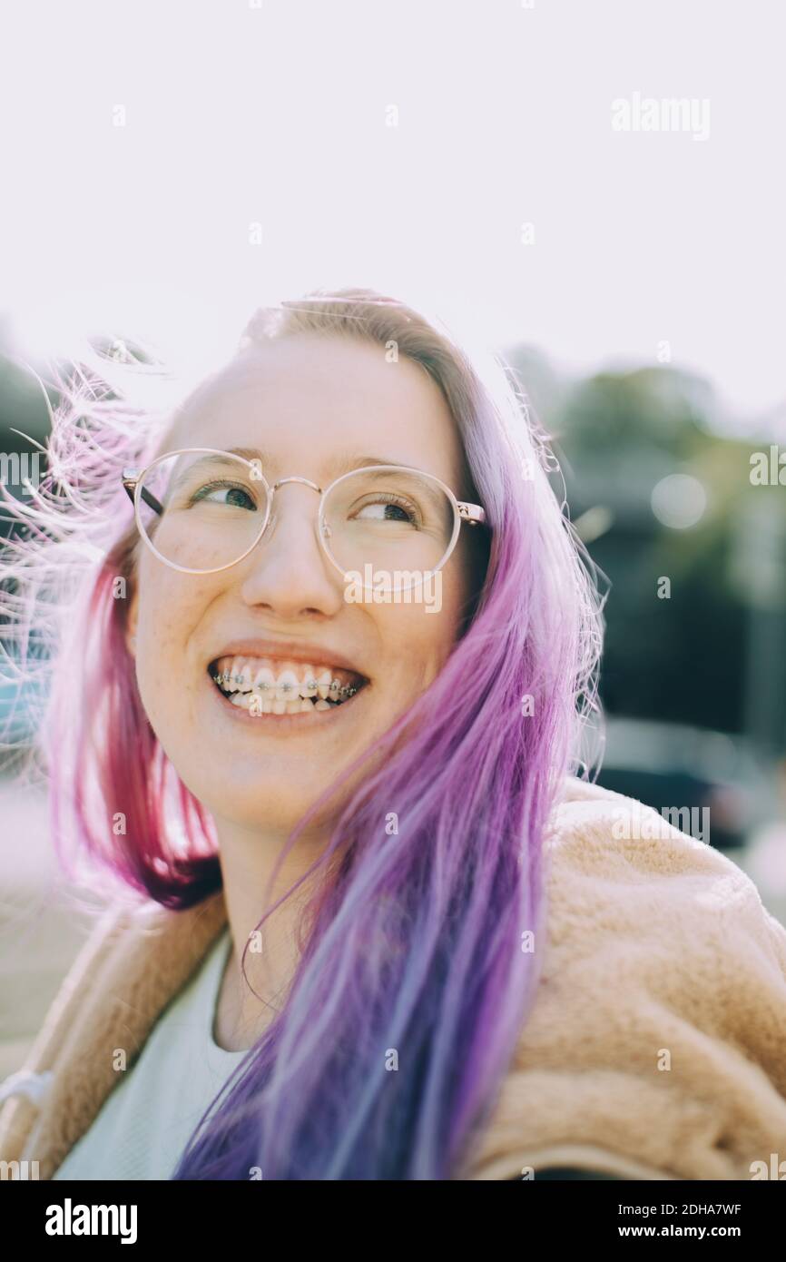 Smiling teenage girl looking away while standing against clear sky Stock Photo