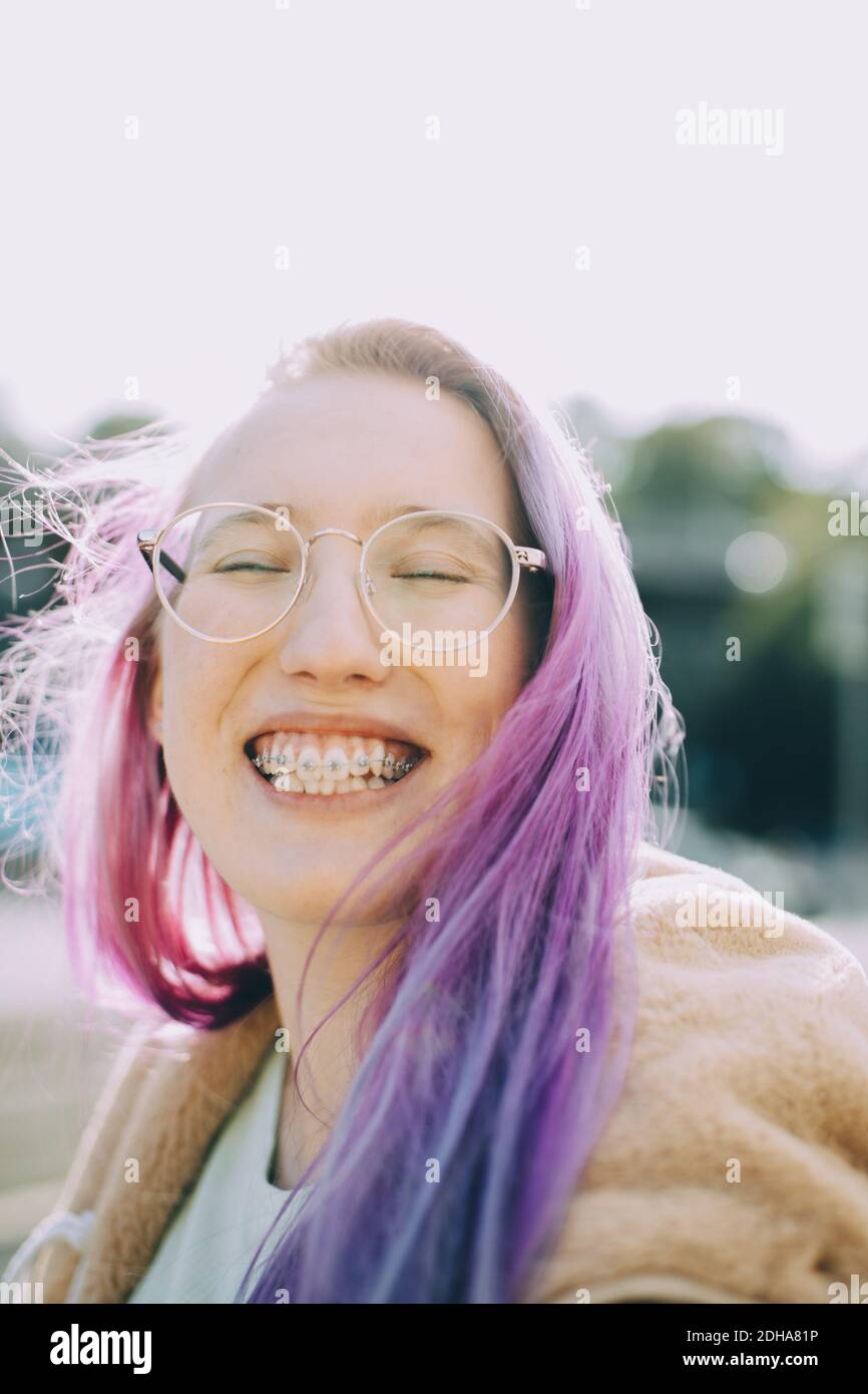 Smiling teenage girl with eyes closed while standing against clear sky Stock Photo