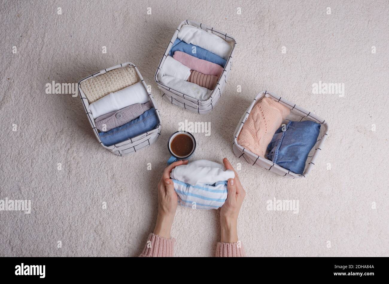 A woman folds clothes and puts them in baskets and boxes. Minimalism in the Scandinavian style. Stock Photo