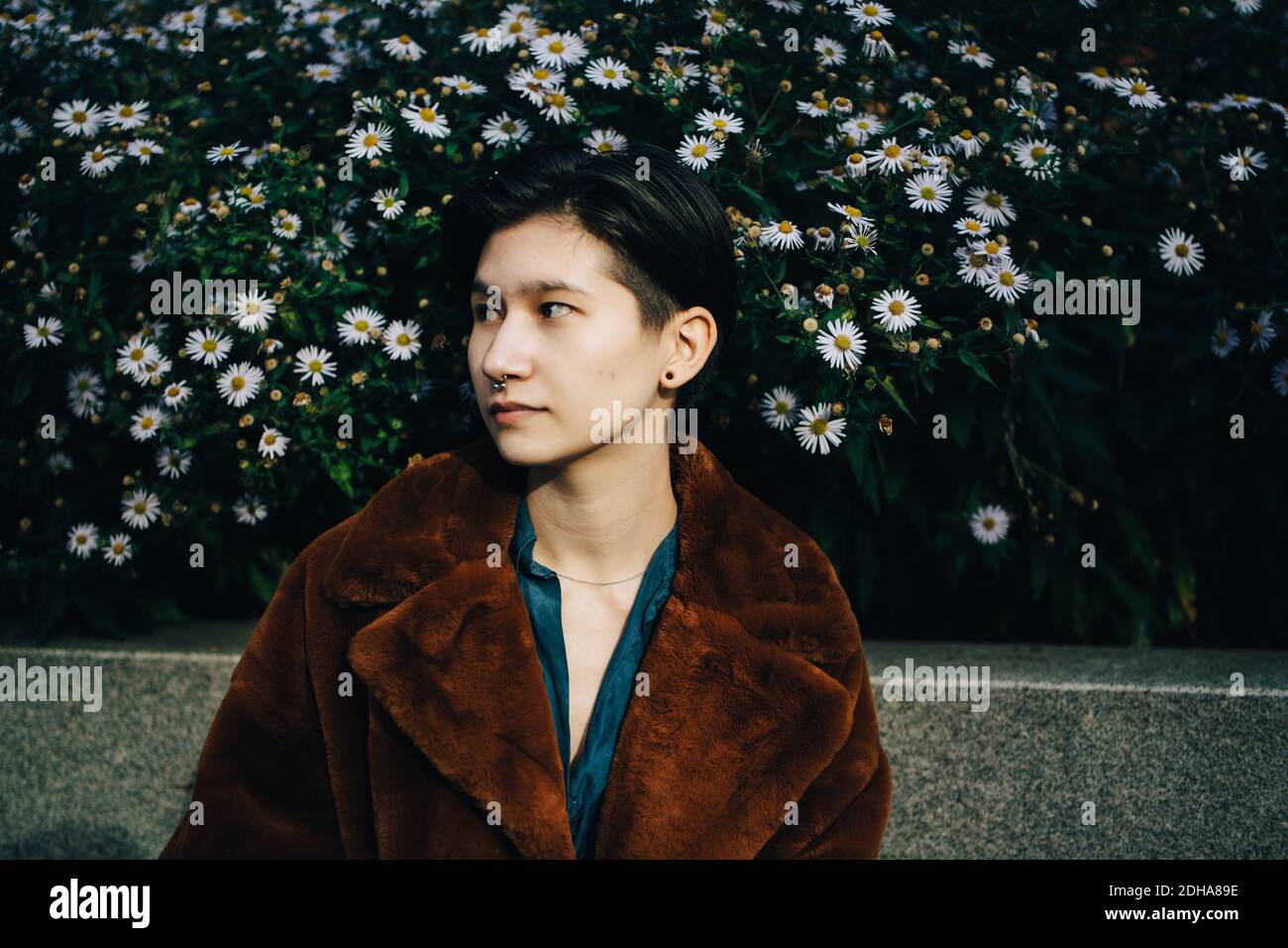 Contemplating woman in jacket standing against daisy flowering plants Stock Photo