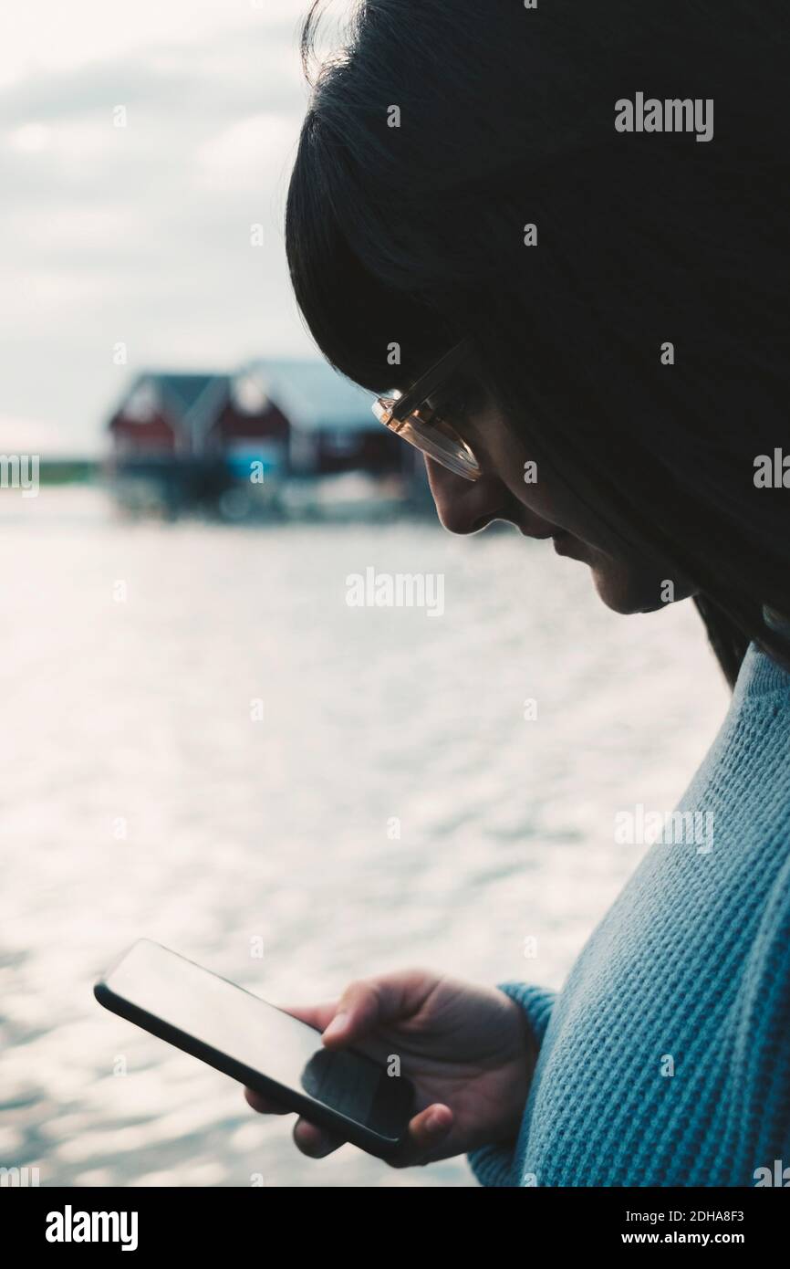 Woman wearing eyeglasses using smart phone by lake Stock Photo