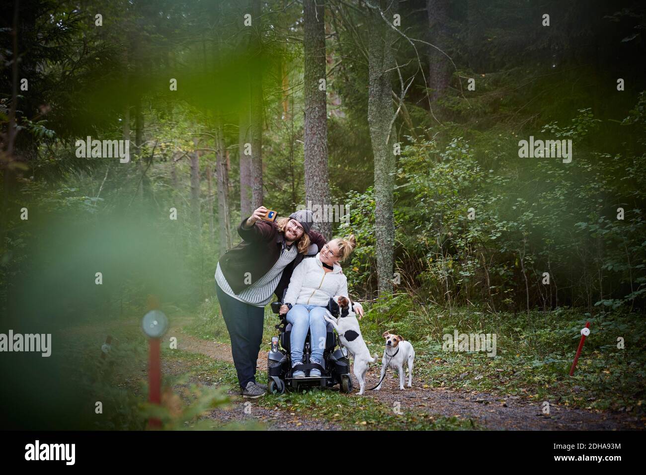 Young male caretaker taking selfie with disabled woman in wheelchair at forest Stock Photo