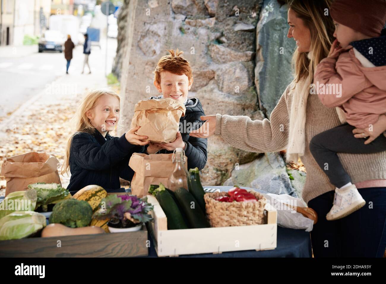 Smiling male and female sibling buying vegetables from female market vendor Stock Photo