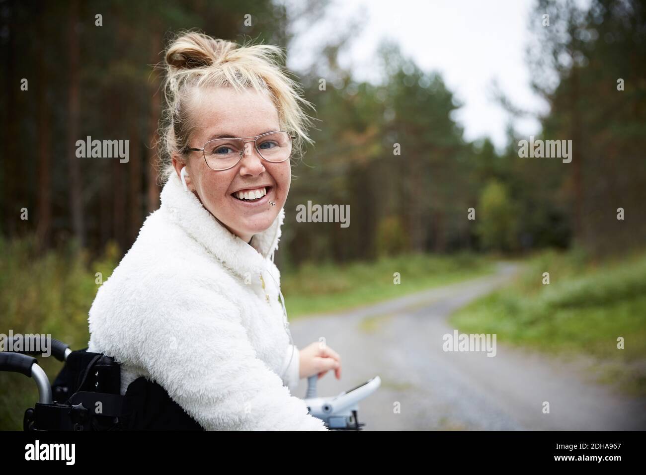 Portrait of smiling young disabled woman sitting in wheelchair on road ...