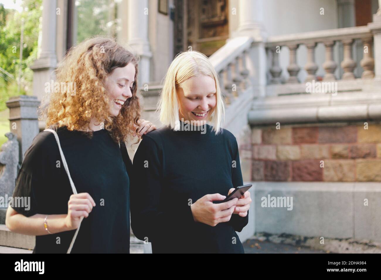 Cheerful young student with female friend using mobile phone by university Stock Photo
