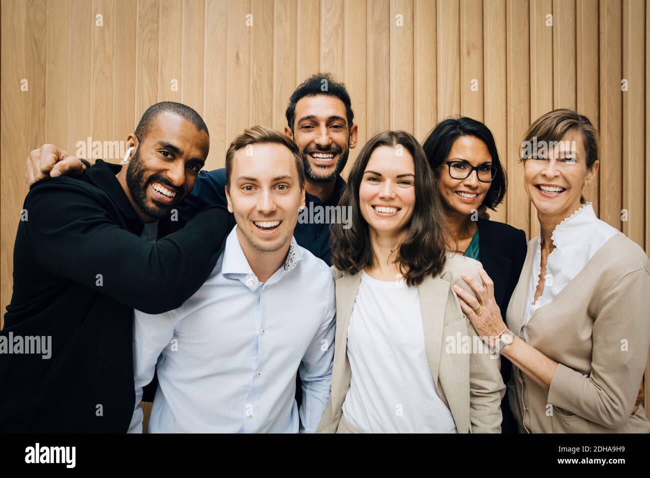 Portrait of happy male and female entrepreneurs standing against wooden ...