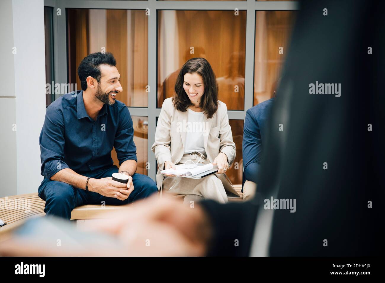 Smiling male and female entrepreneurs talking while sitting against office Stock Photo