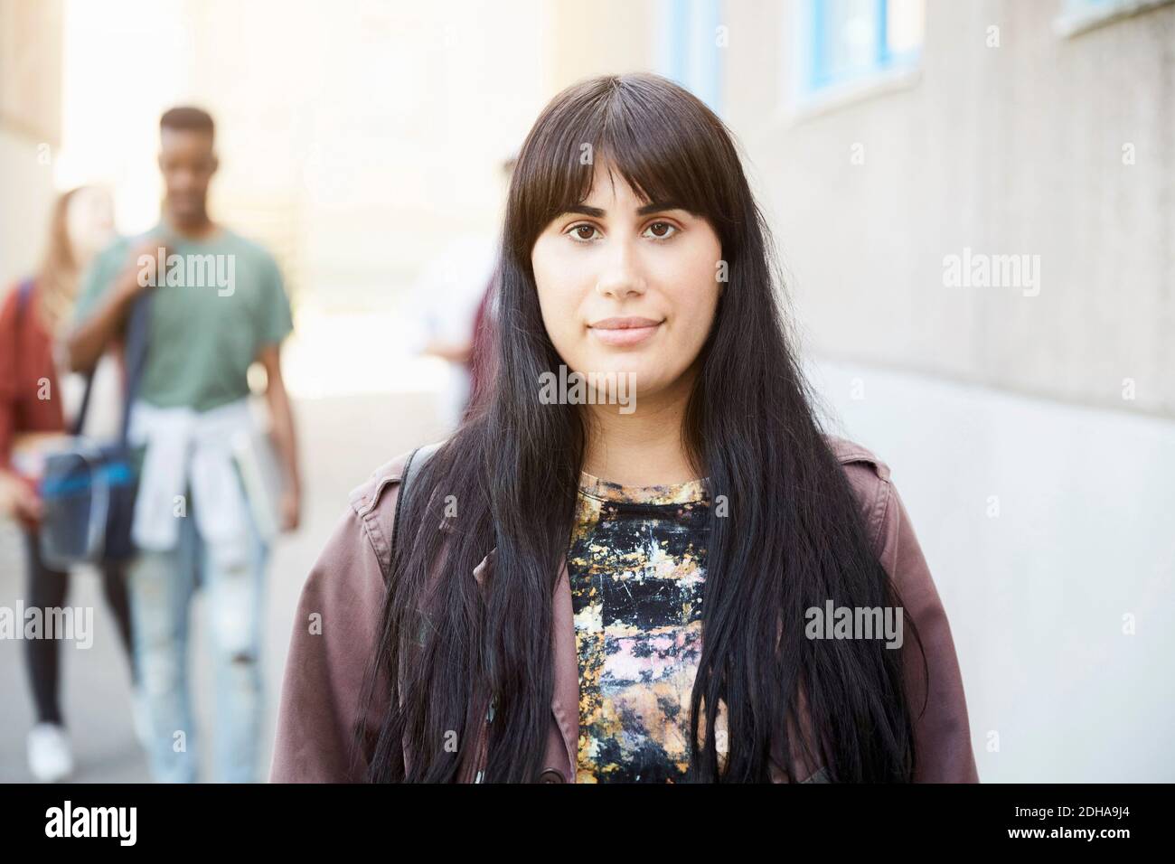 Portrait of young woman with long hair standing at university campus with friends in background Stock Photo
