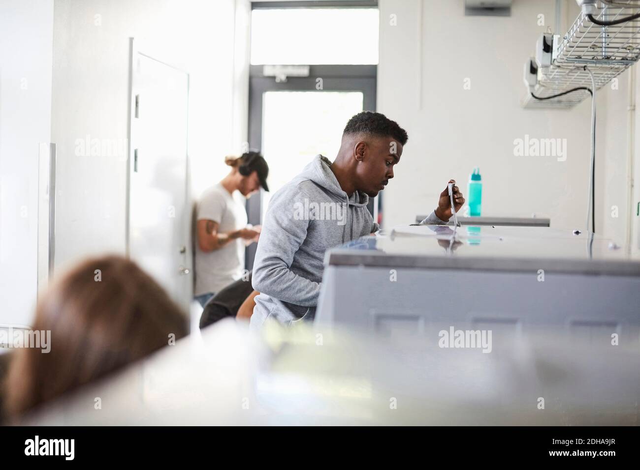 Young man using washing machine in campus laundromat Stock Photo