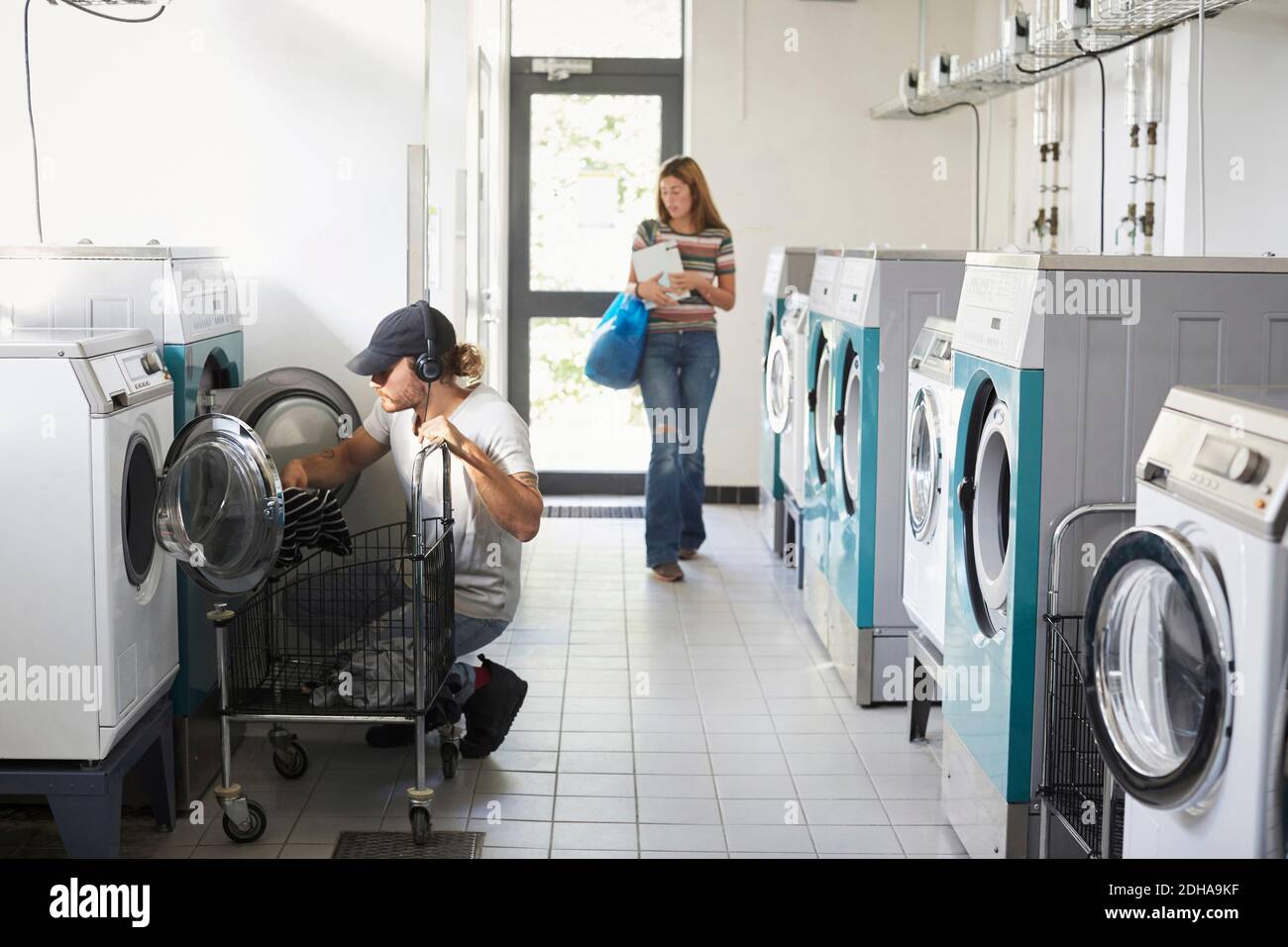 Man using washing machine while woman walking in laundromat Stock Photo