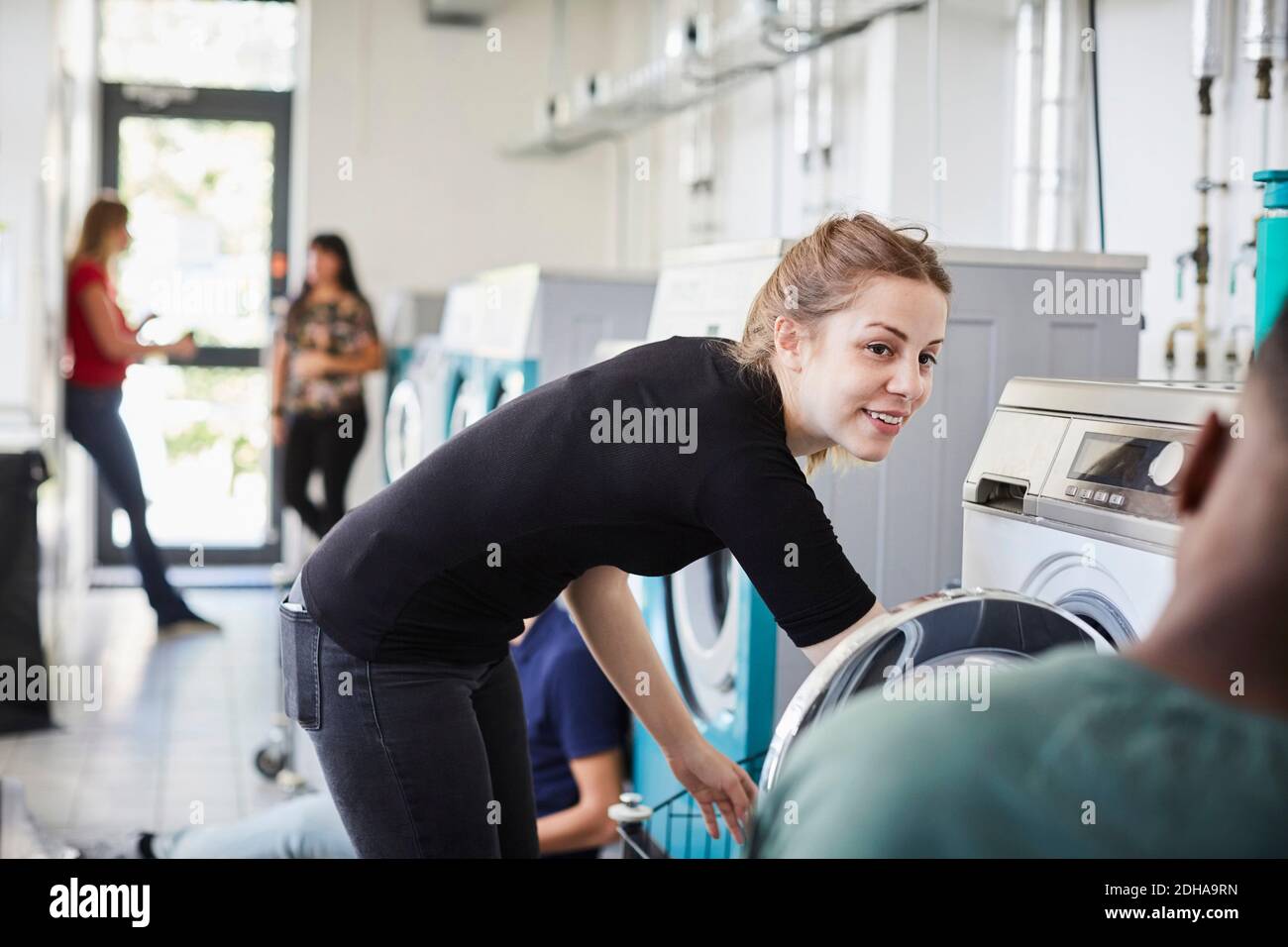Smiling woman looking at friend while doing laundry Stock Photo