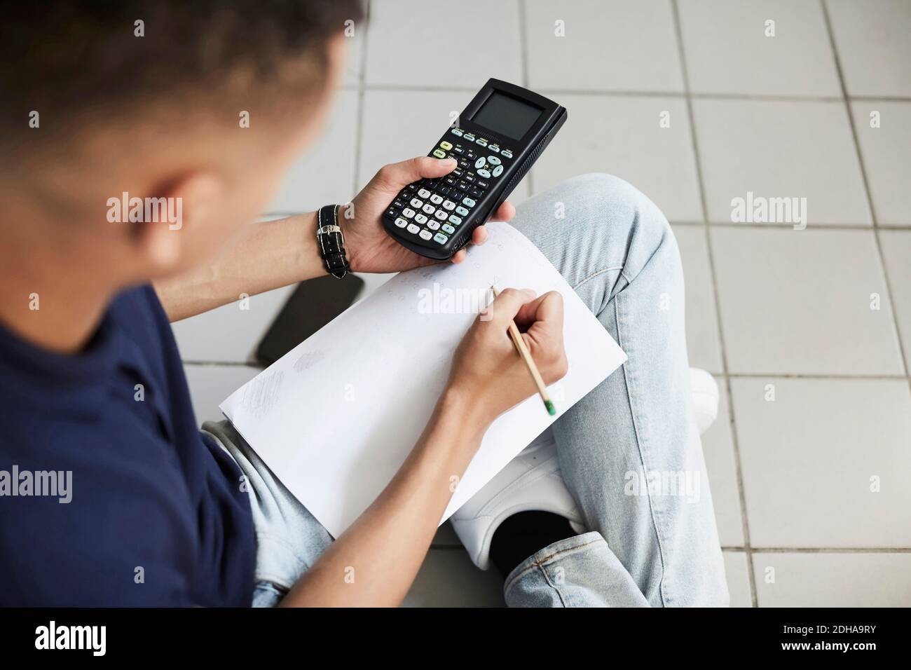 Young man using calculator and writing on paper while sitting with crossed legs at laundromat Stock Photo