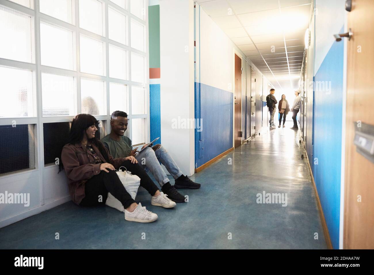 Friends using digital tablet while students standing in corridor at university Stock Photo