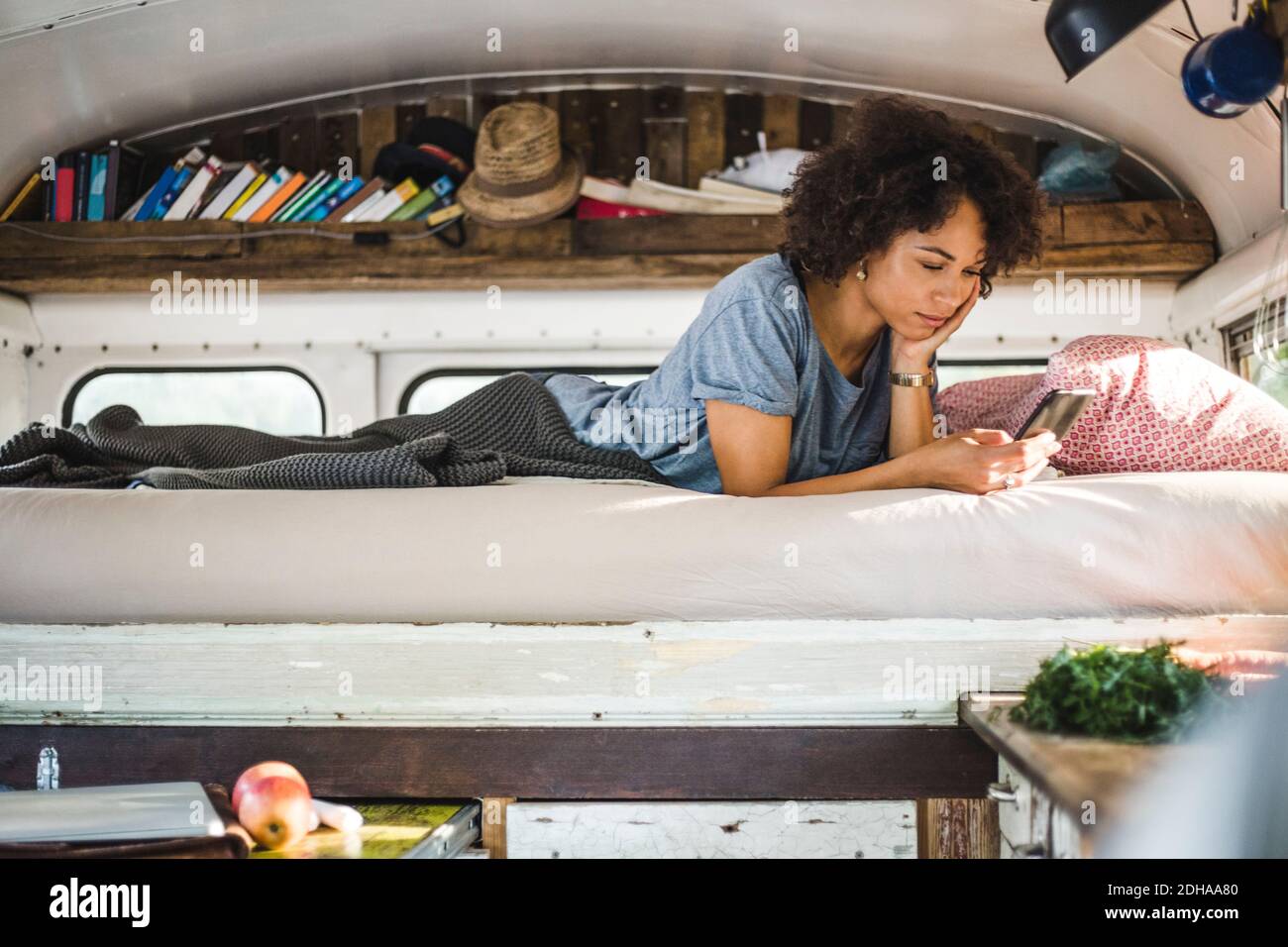 Young Afro woman surfing through mobile phone while lying on bed in motor home Stock Photo