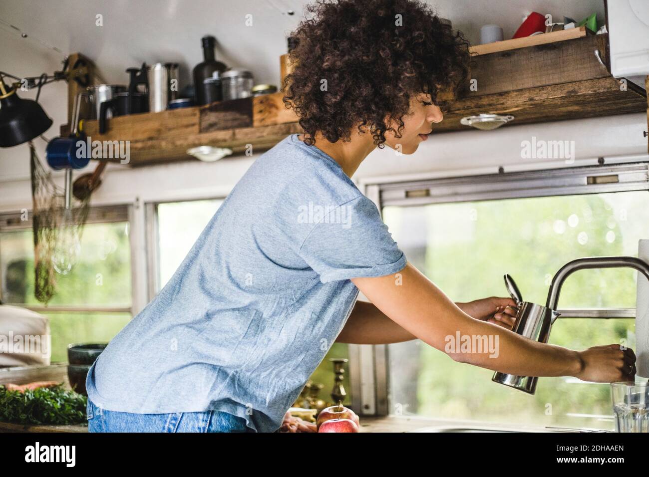 Side view of Afro woman filling kettle from faucet in motor home Stock Photo