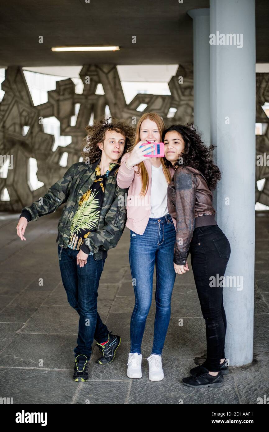 Full length of friends taking selfie from smart phone by column at parking garage Stock Photo
