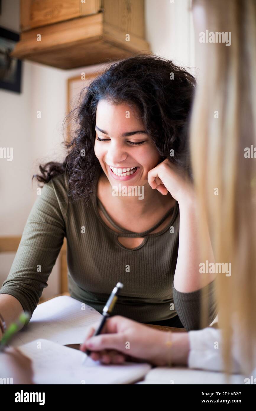 Smiling teenage girl doing homework with female friend at home Stock Photo
