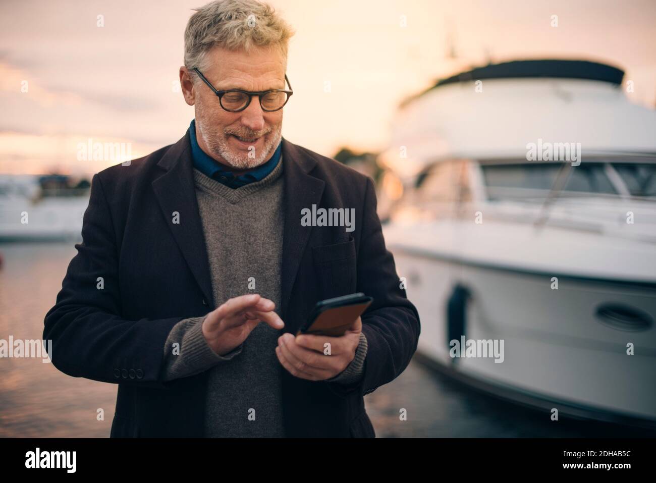 Senior man using smart phone while standing at harbor Stock Photo