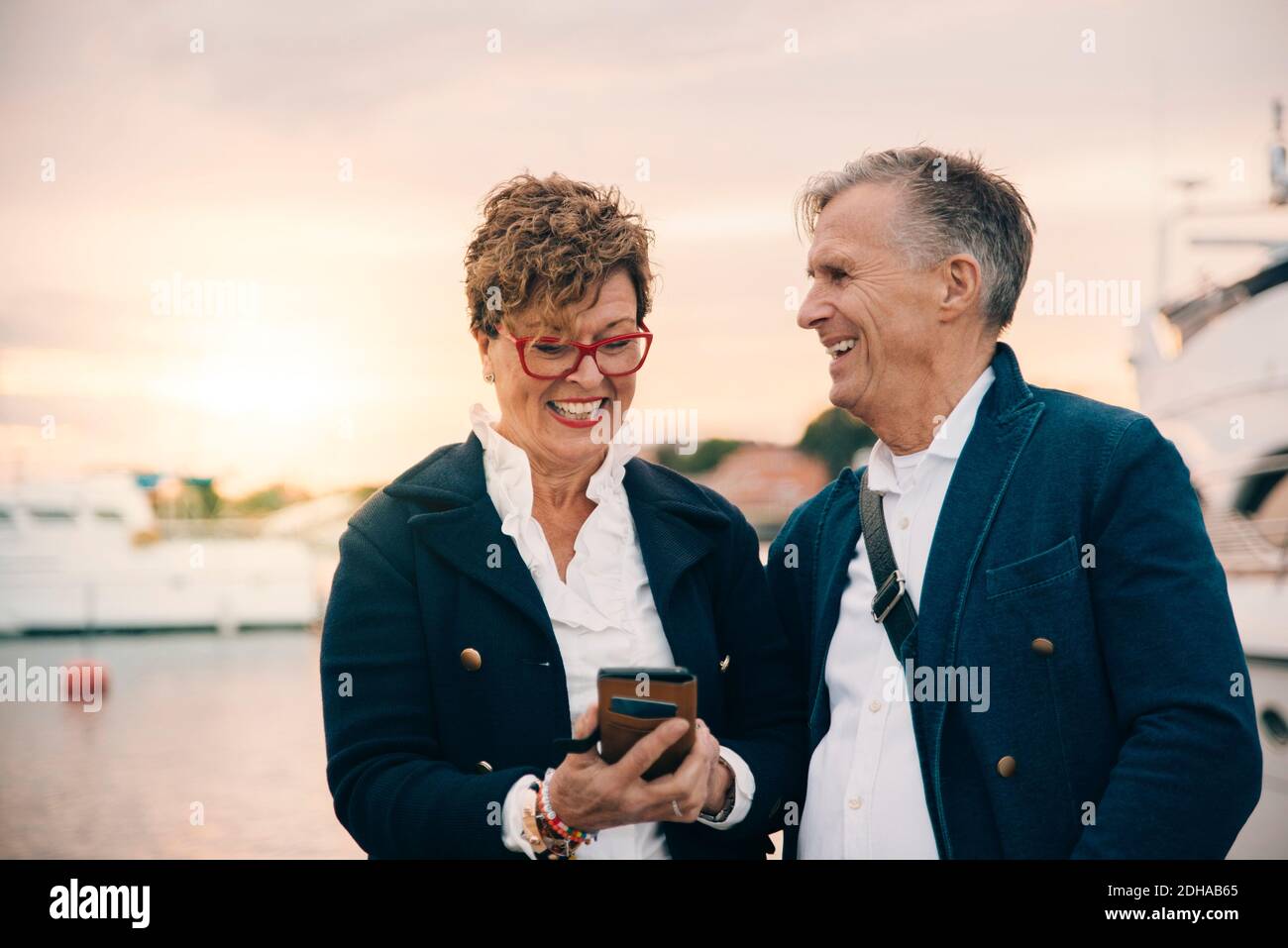 Happy senior woman using smart phone while standing by man at harbor Stock Photo