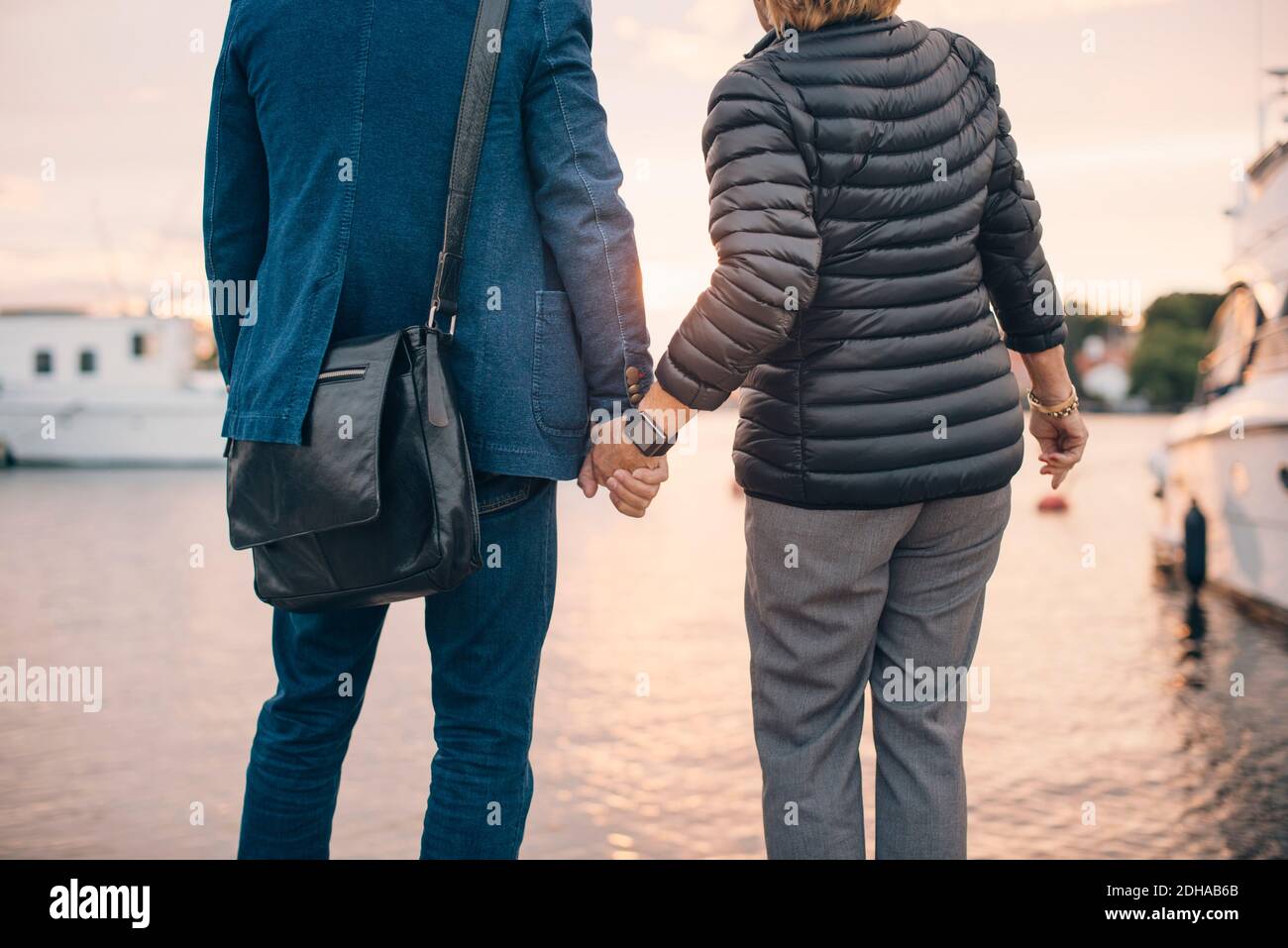 Midsection of senior couple holding hands while standing at harbor Stock Photo