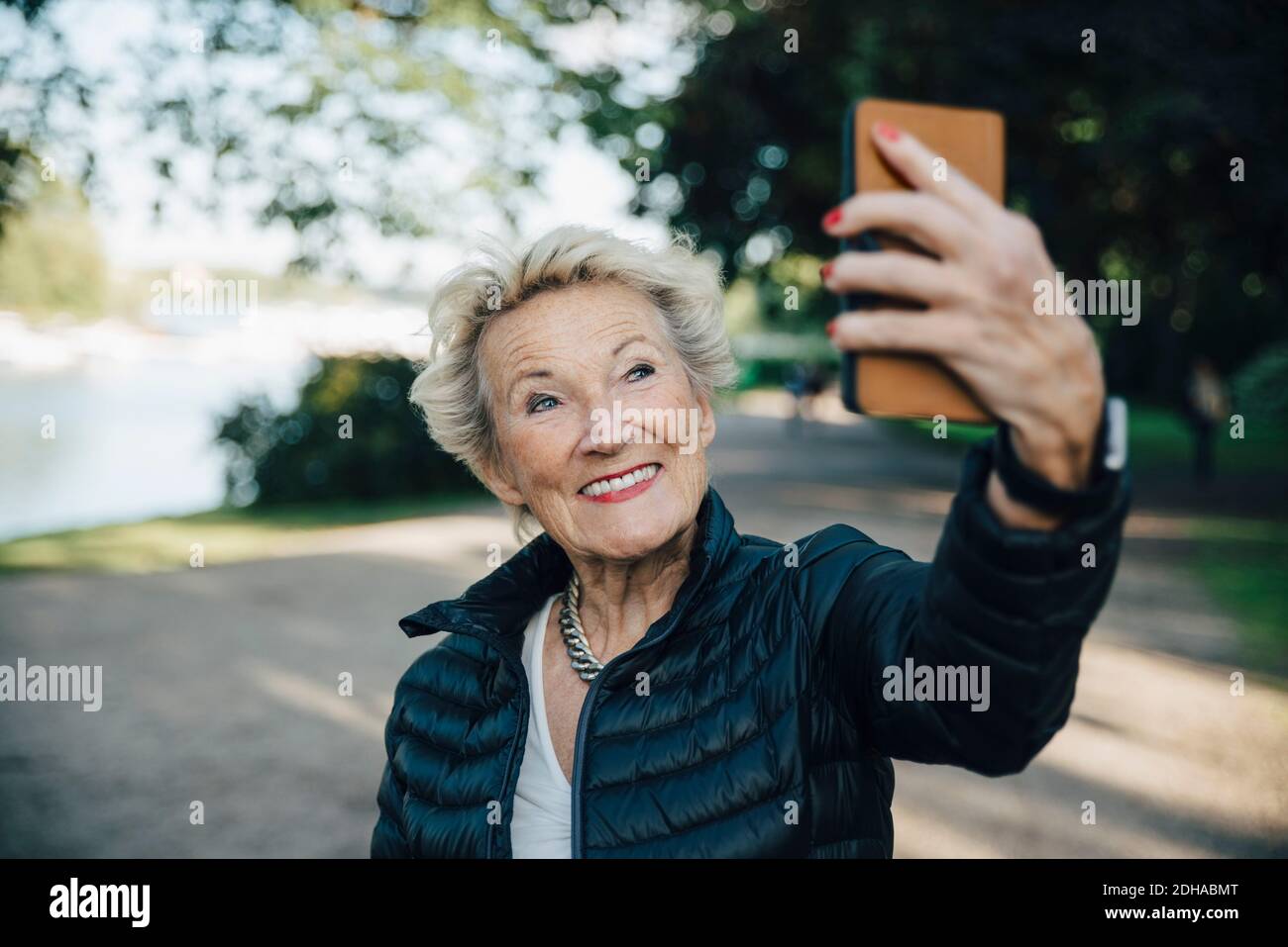 Smiling senior woman taking selfie with smart phone in park Stock Photo