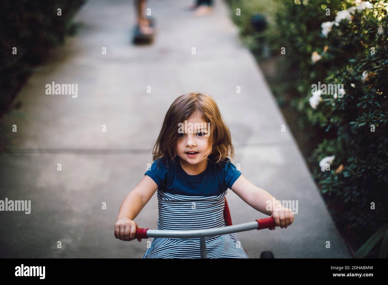 Girl riding tricycle on footpath Stock Photo
