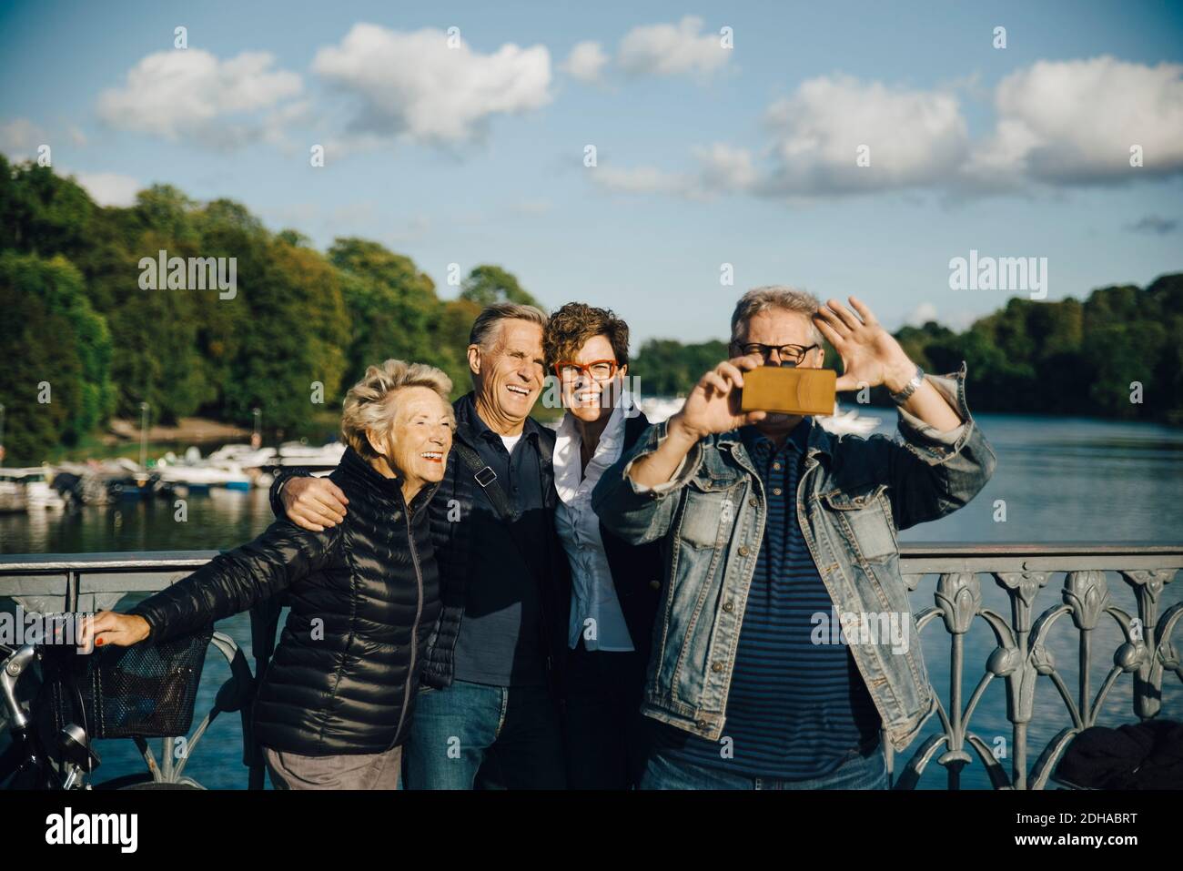 Smiling male and female friends taking selfie with smartphone by railing of bridge Stock Photo