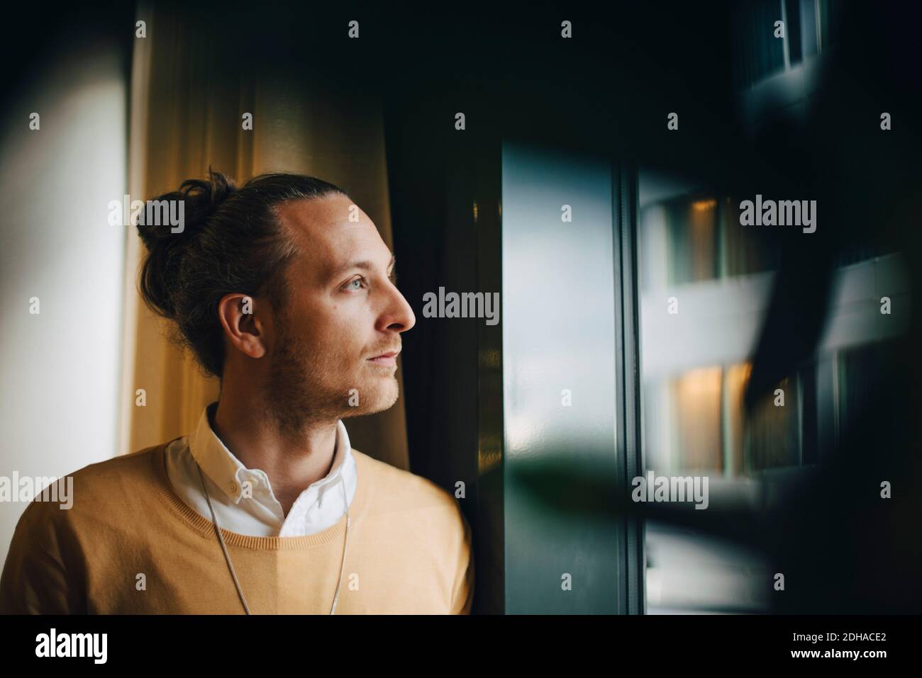 Thoughtful businessman looking through window standing at office Stock Photo
