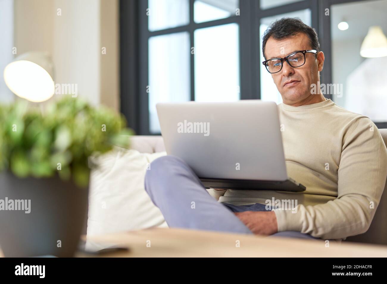 Portrait of latin middle aged business man with eyeglasses working at home on some project, sitting on a sofa with his laptop. Focus on the man. Telework, business concept Stock Photo