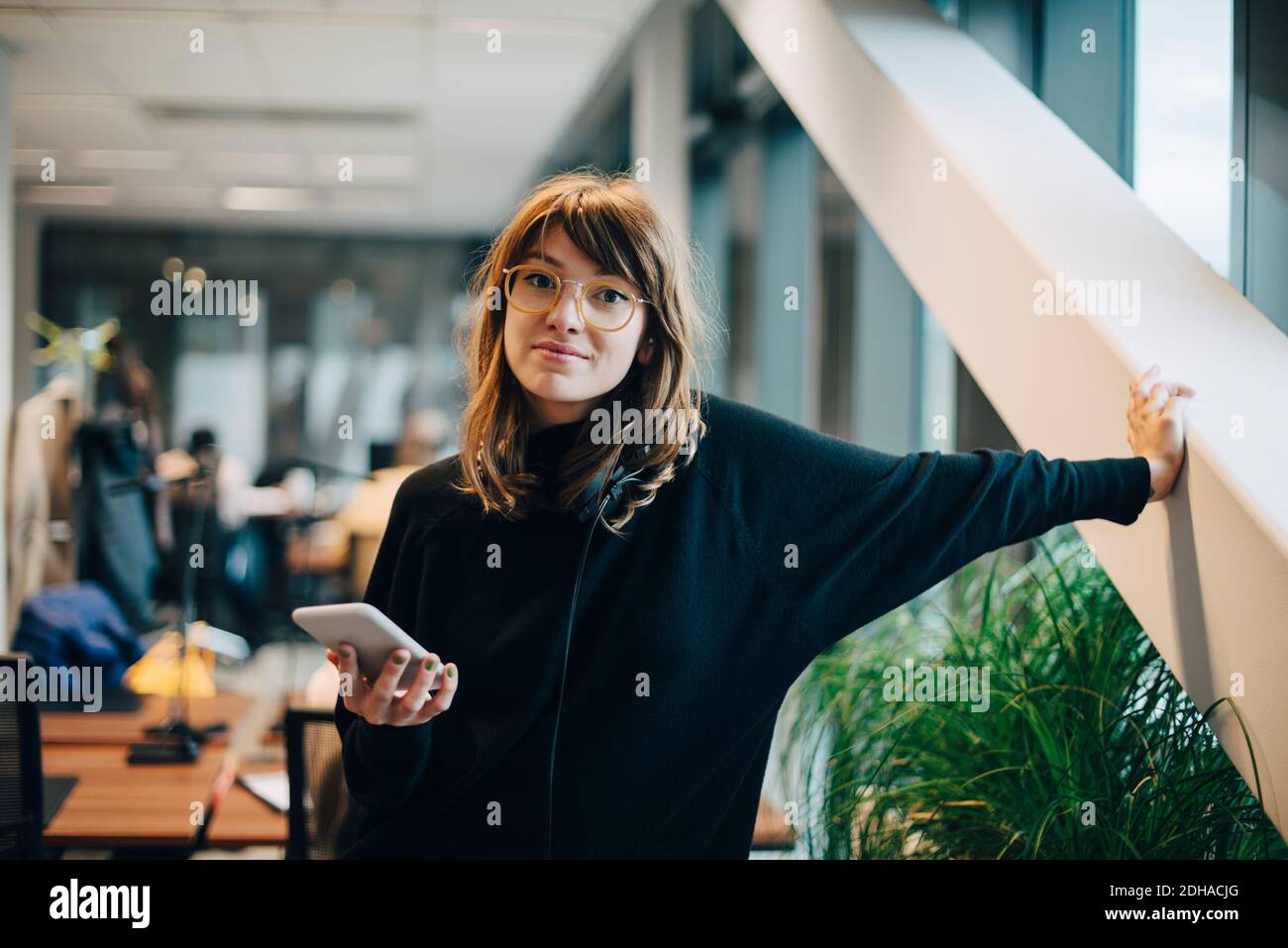 Portrait of confident businesswoman standing with smart phone in office Stock Photo