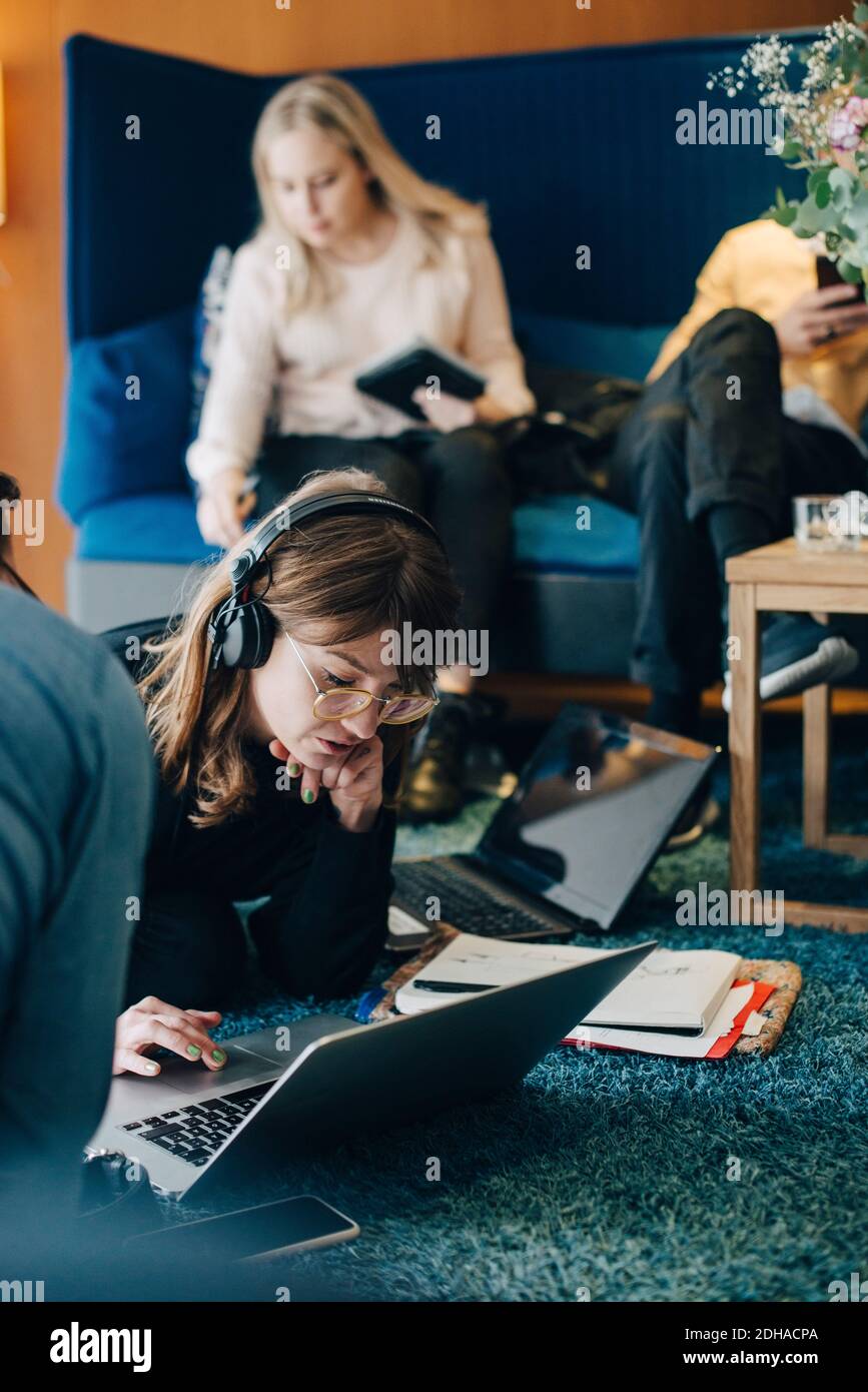 Young businesswoman using laptop while sitting amidst colleagues in cafeteria at office Stock Photo