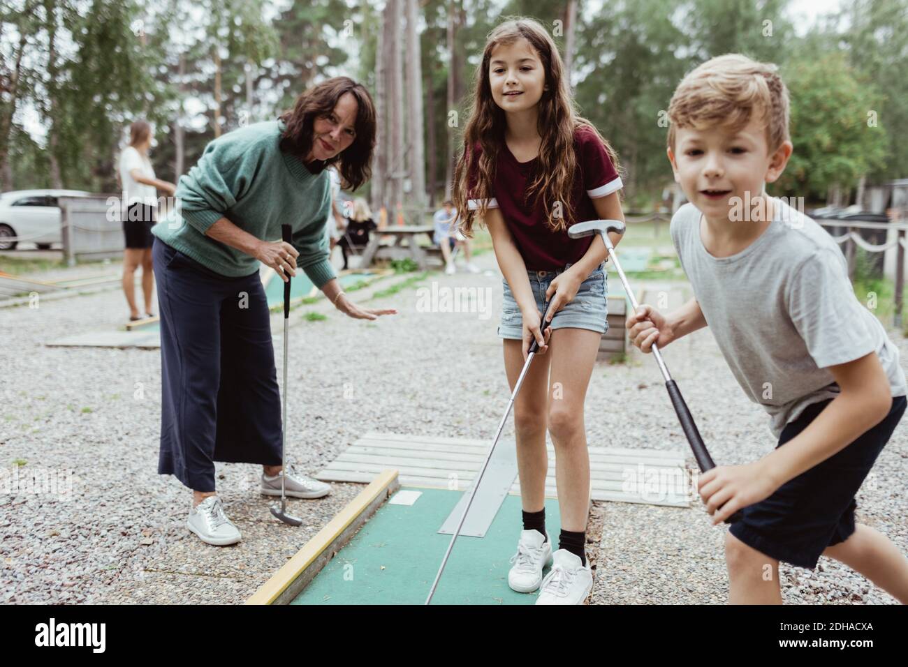 Sibling playing miniature golf with family in backyard during vacation Stock Photo